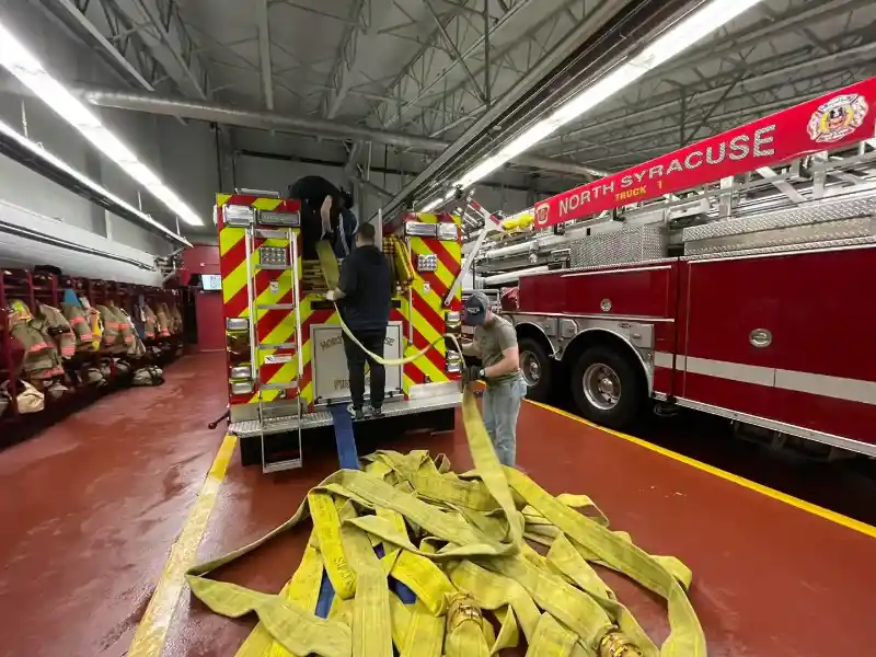 Fire fighters fixing the hose on the back of the fire truck in the firehouse